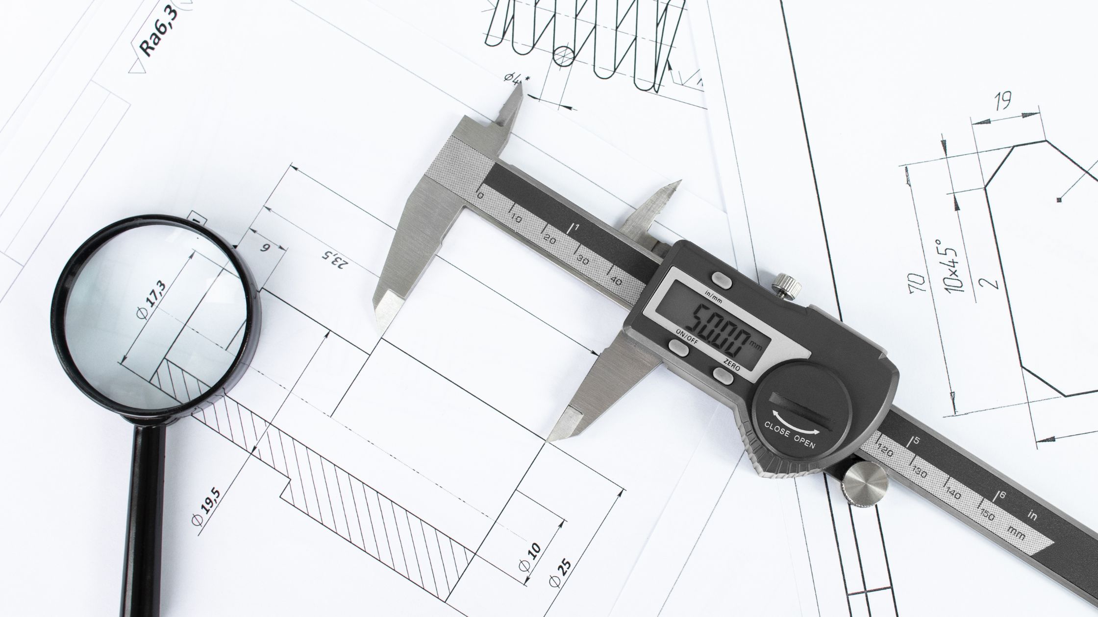 Digital caliper and magnifying glass on dimensional engineering drawings