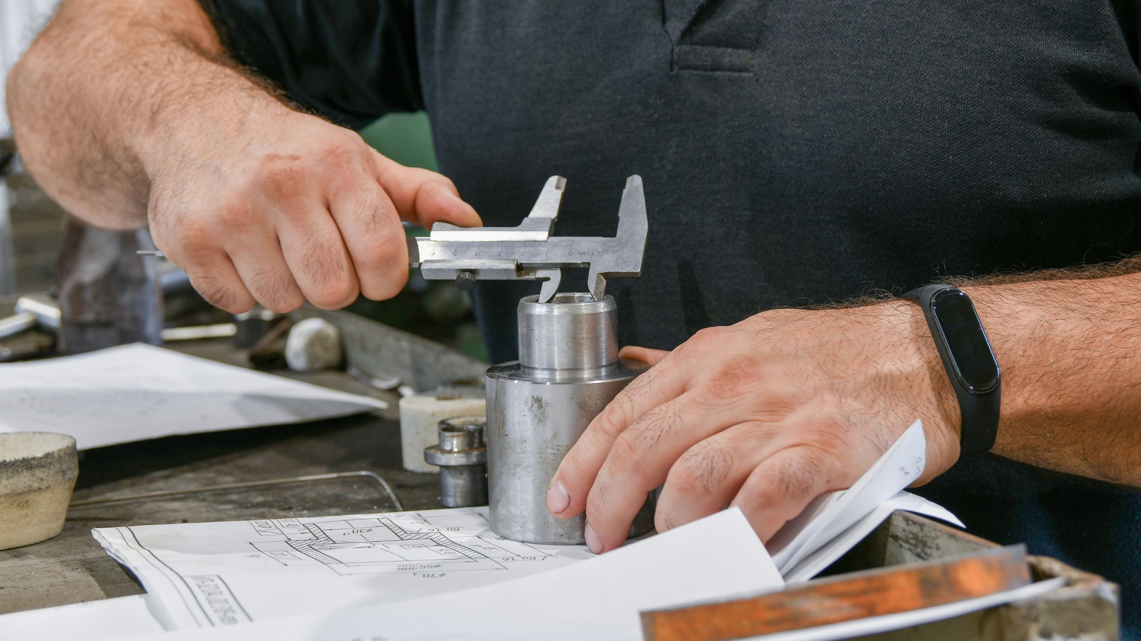 Engineer measuring machined component against technical drawing in workshop